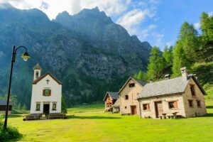 Idyllic village scene with chapel and houses set against the Monte Rosa mountains in Lombardia, Italy.